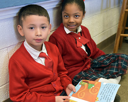Two school children read a book together.